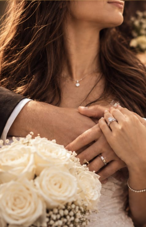 Joined hands with wedding rings and white roses